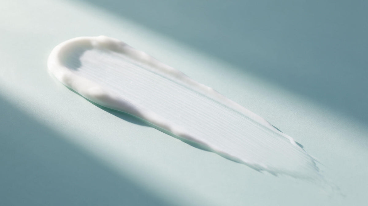 A sheer smear of white sunscreen on a pale aqua surface in direct sunlight
