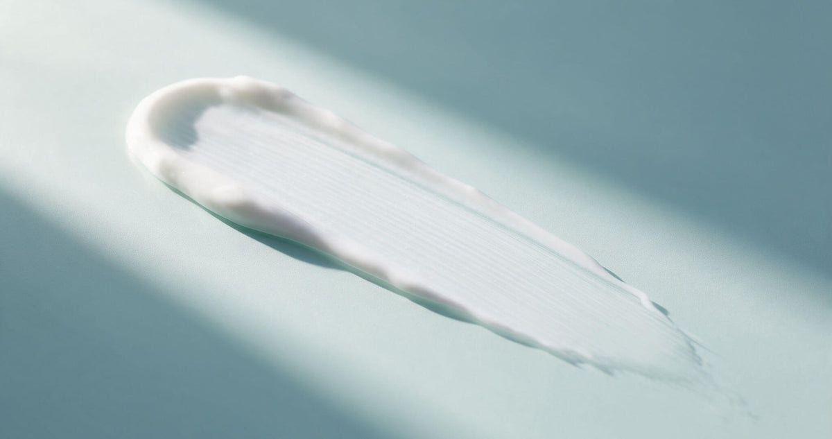 A sheer smear of white sunscreen on a pale aqua surface in direct sunlight