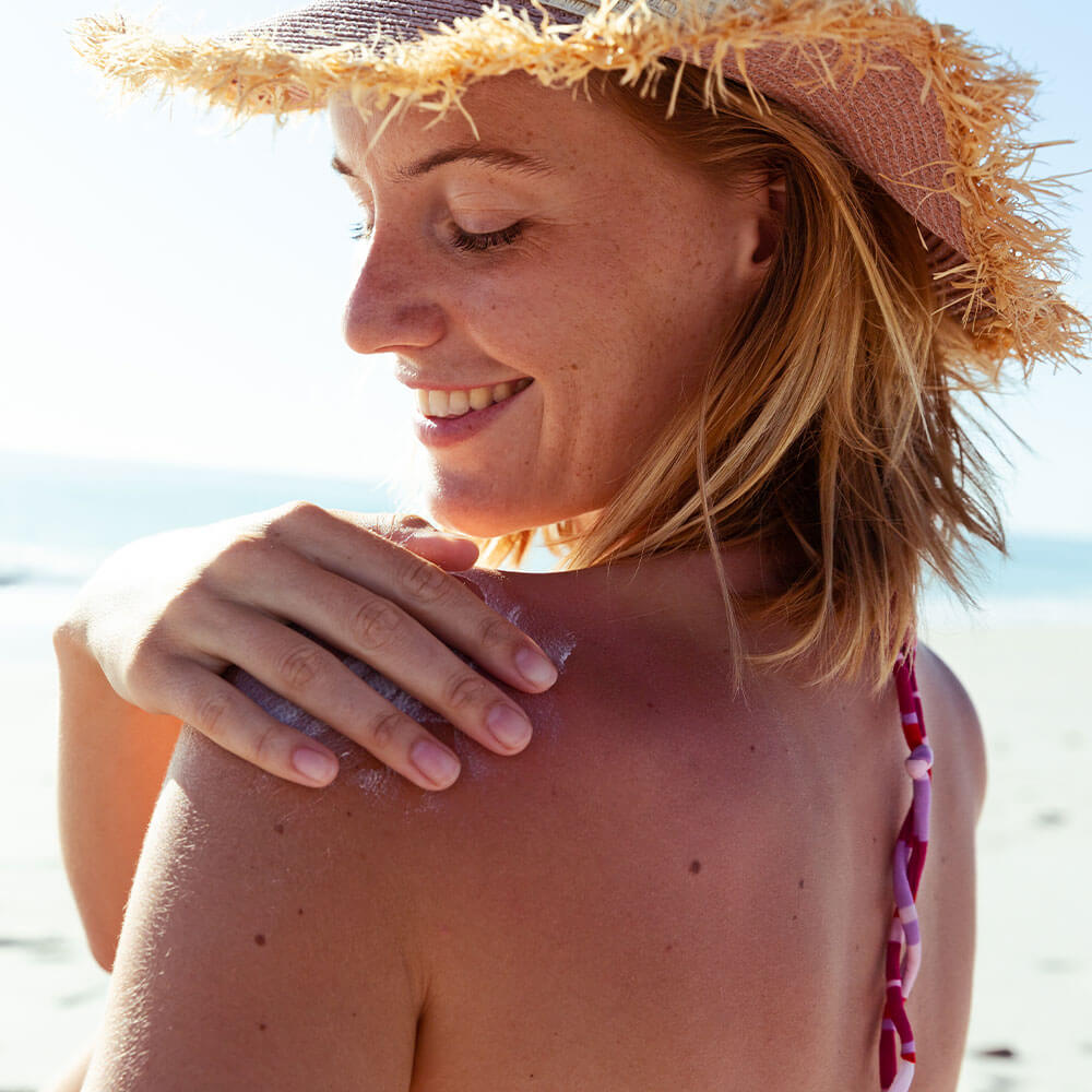 Woman applying SolRX mineral sunscreen to shoulder beach lifestyle no white cast